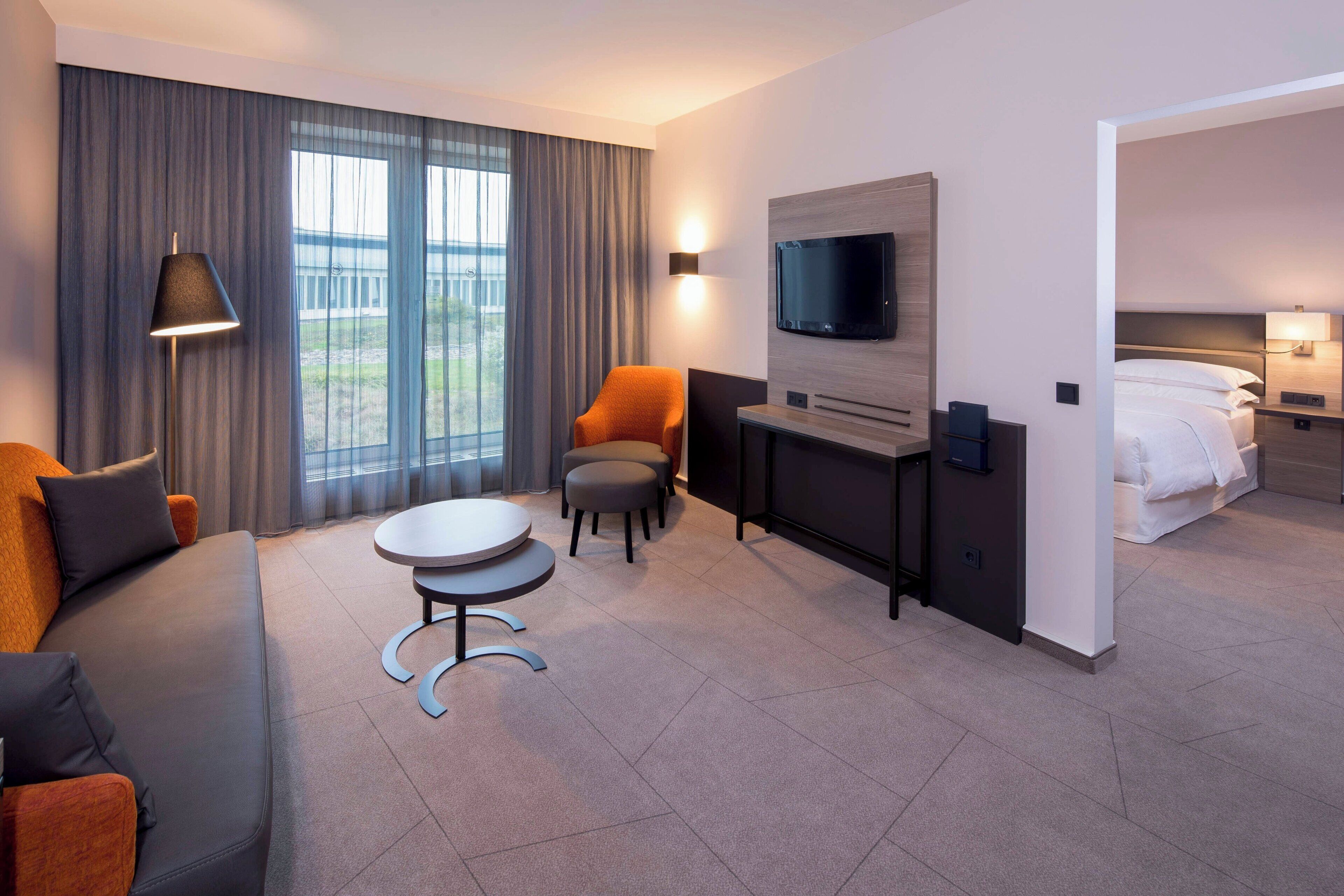 Habitación de hotel con sofá, sillón, mesita, televisión y cama.
