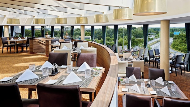 A modern restaurant with high ceilings, large windows, and a view of the cityscape. - Sheraton Duesseldorf Airport Hotel (Düsseldorf)