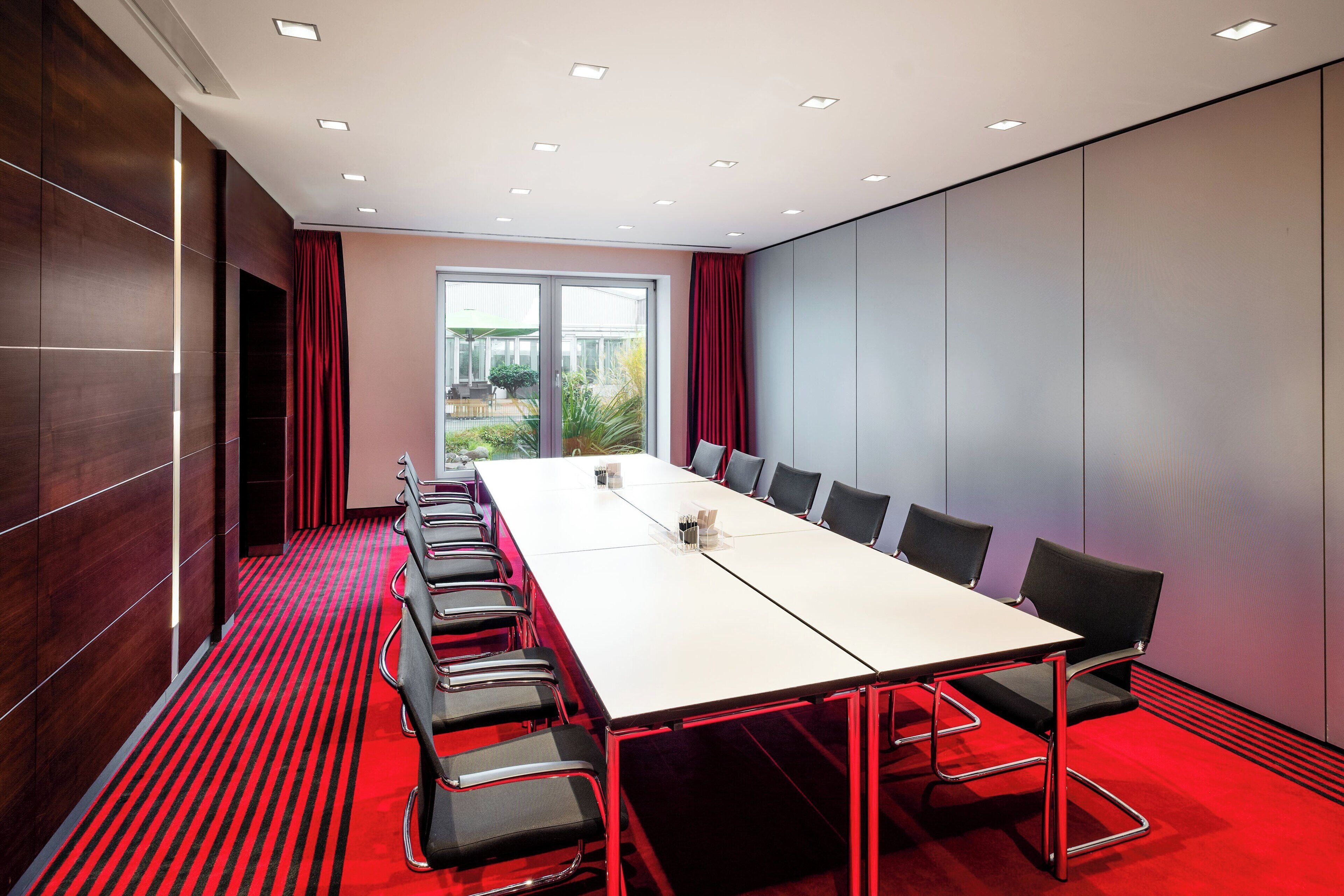 Une salle de conférence avec une longue table, des chaises et une vue sur l’extérieur grâce à une porte vitrée.