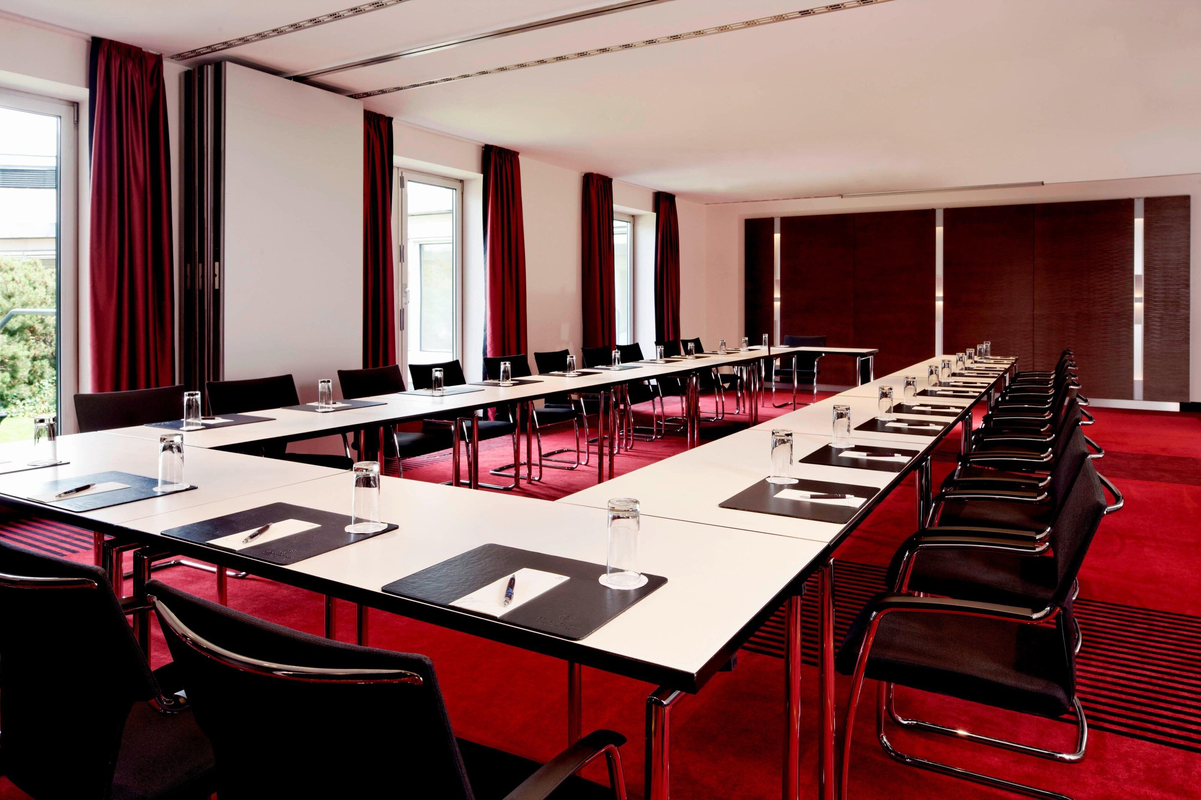 Un salón de conferencias con una larga mesa, sillas y amplias ventanas con cortinas.