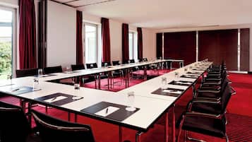 Un salón de conferencias con una larga mesa, sillas y amplias ventanas con cortinas.