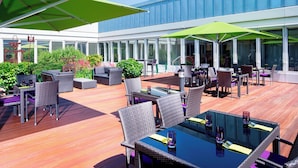 An outdoor patio area with wicker furniture, glass tables, and umbrellas. - Sheraton Duesseldorf Airport Hotel (Düsseldorf)