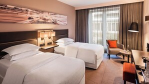A hotel room with two beds, a desk, a chair, a lamp, and a large window with curtains. - Sheraton Duesseldorf Airport Hotel (Düsseldorf)