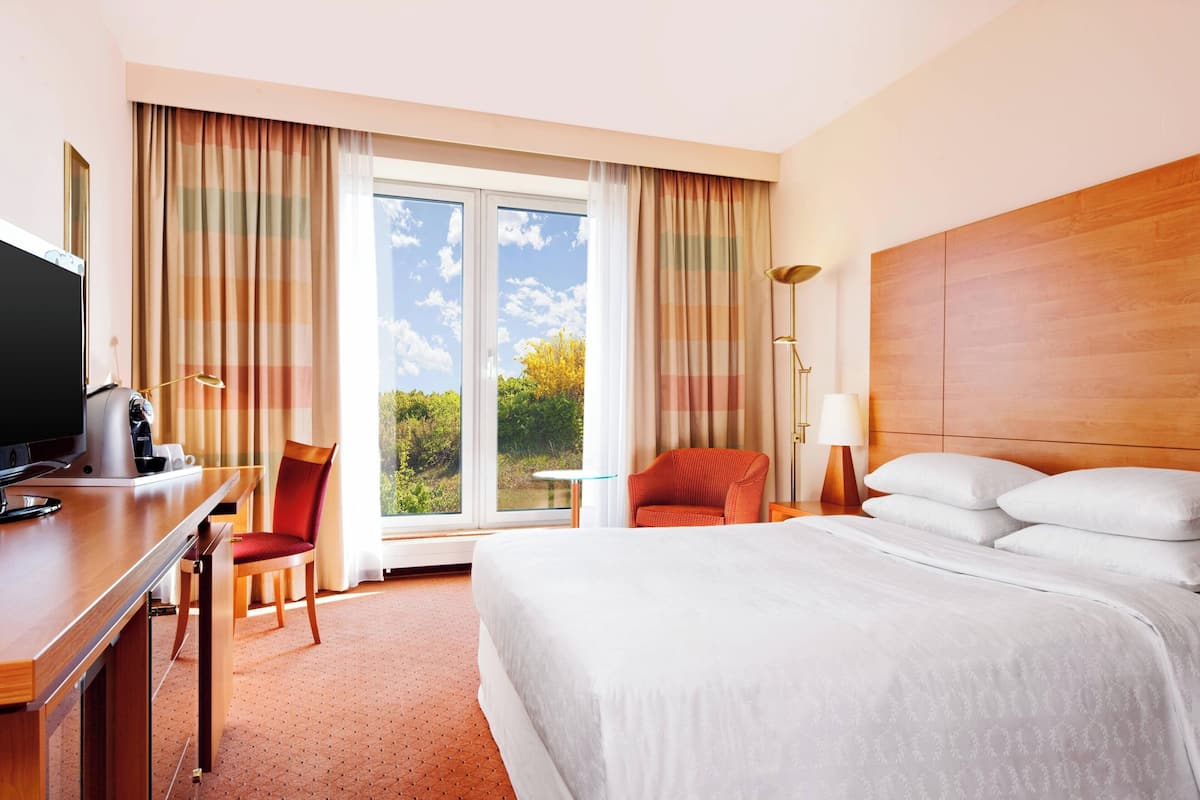 Habitación de hotel con cama, escritorio con computadora, silla, lámpara y vistas al exterior.