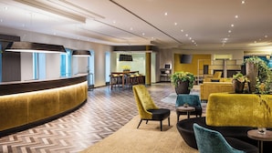 A modern hotel lobby with a curved reception desk, seating area with plush chairs, and a herringbone patterned floor. - Sheraton Duesseldorf Airport Hotel (Düsseldorf)