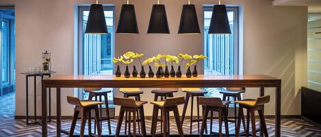 Un espace de salle à manger moderne, avec une longue table, six chaises et des lampes suspendues.