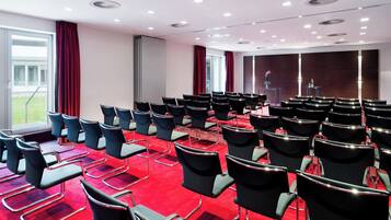 Une salle de conférence avec des rangées de chaises, un pupitre et une grande fenêtre.