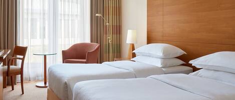 Habitación de hotel con dos camas, una silla, una mesa y una lámpara.