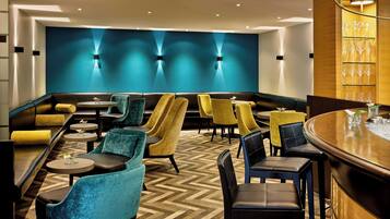 Un espace de détente moderne avec un parquet en chevrons, un bar et différents types de sièges, notamment des canapés et des fauteuils.