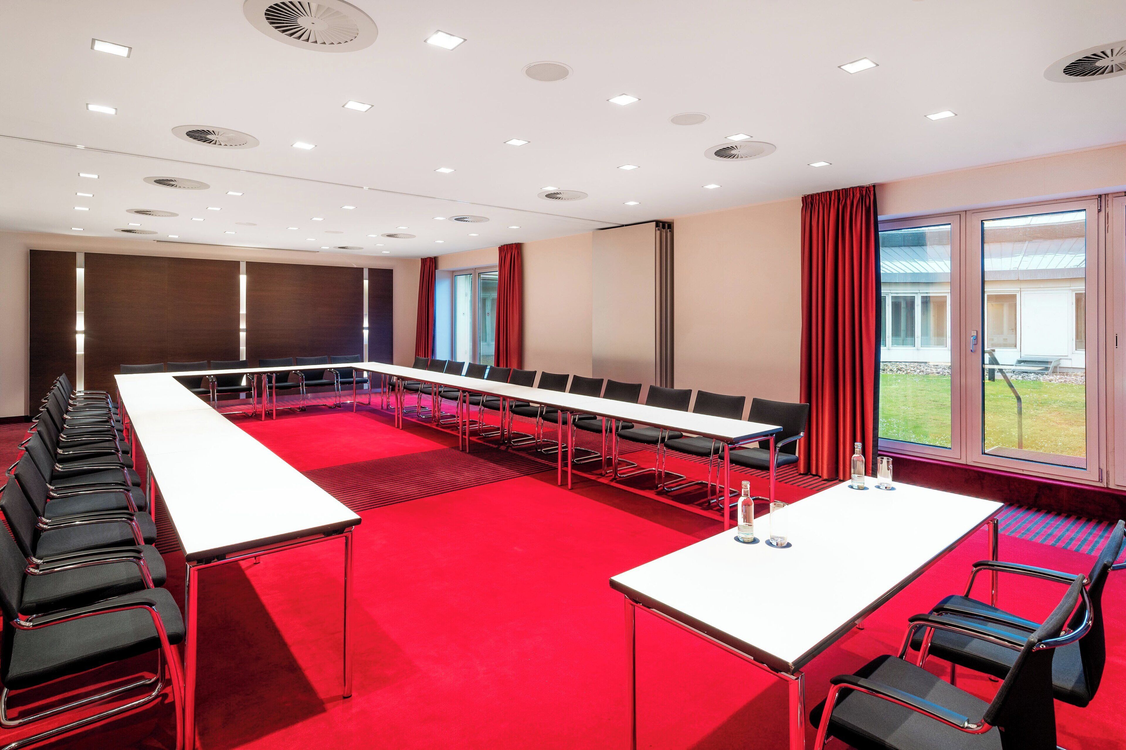 Un salón de conferencias con una larga mesa, sillas y una alfombra roja.