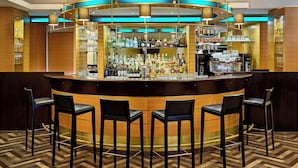 A bar area with a curved counter, multiple bar stools, and shelves stocked with bottles and glasses. - Sheraton Duesseldorf Airport Hotel (Düsseldorf)