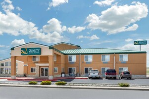 Edificio de Quality Inn & Suites de dos pisos, con área de estacionamiento techada y cielo despejado con nubes.