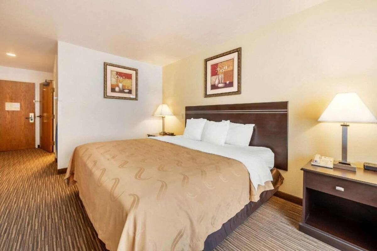 A hotel room with a large bed, two bedside lamps, a nightstand, and two framed pictures on the wall.