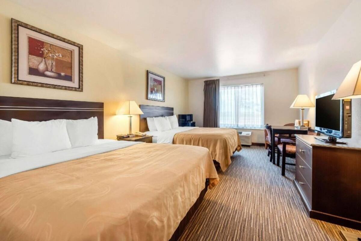 A hotel room with two beds, a desk, a television, and a window with curtains.