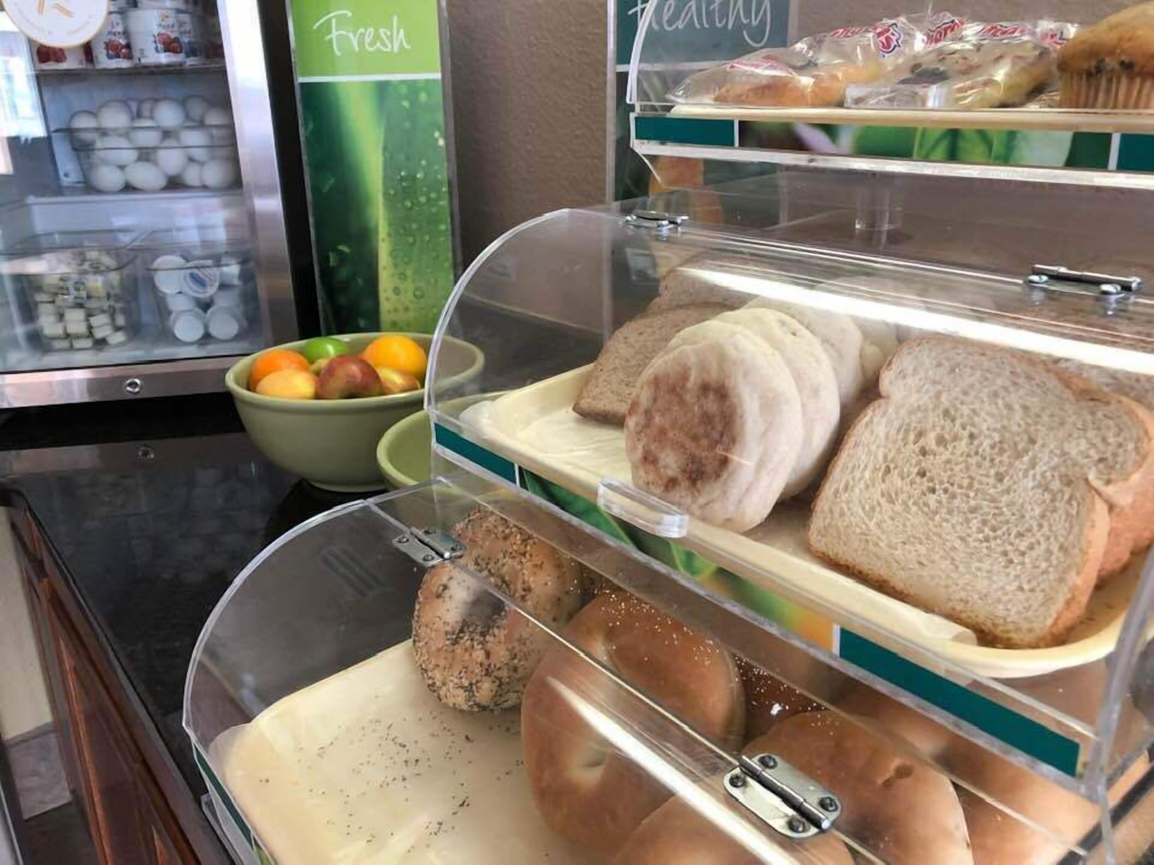 A bakery display case with bread, muffins, and a bowl of fruit.