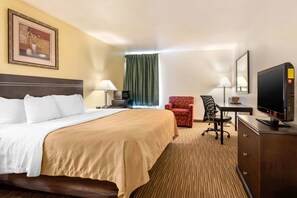 A hotel room with a large bed, a desk with a computer, a television, and a chair.