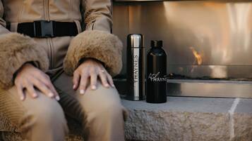 A person sitting by a fireplace with two black water bottles and a stainless steel thermos.