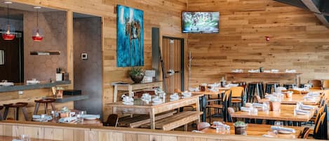 A restaurant with wooden walls and hexagonal patterns, tables set with white tableware, and a TV mounted on the wall.
