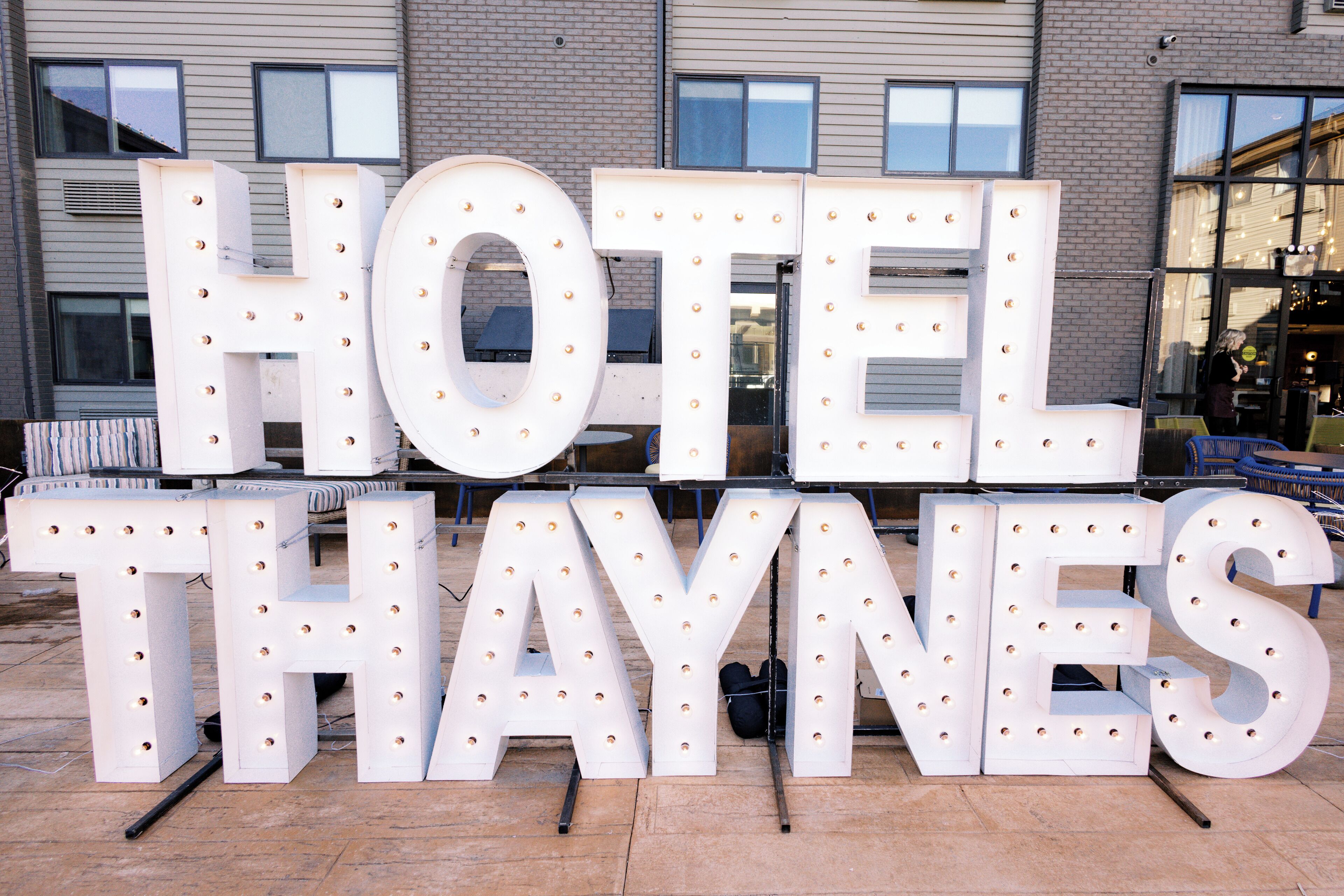 Large illuminated letters spelling "HOTEL THAYNES" in front of a building.