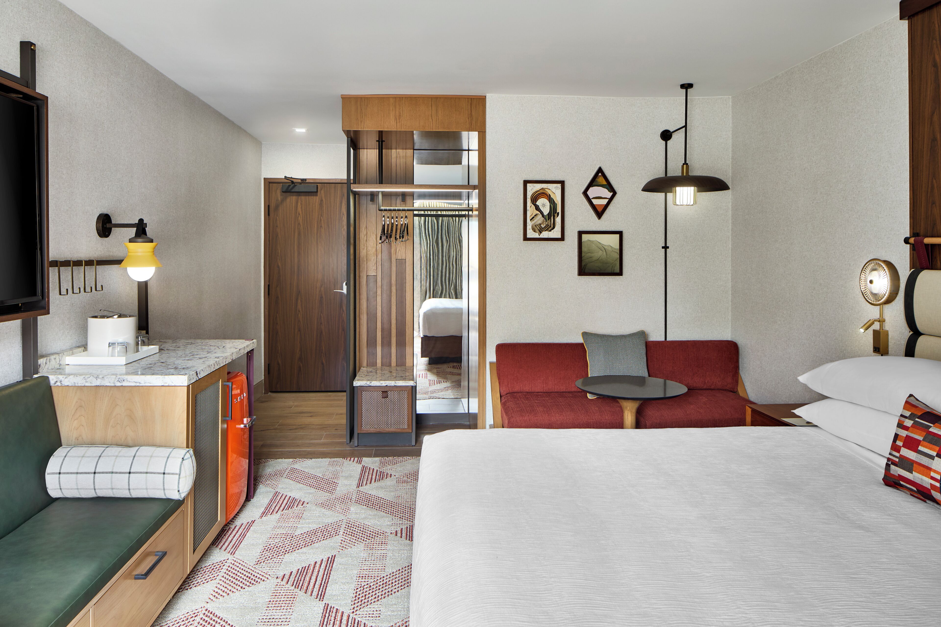 Habitación de hotel con cama, sofá, escritorio con lámpara, televisor y zona de ducha.
