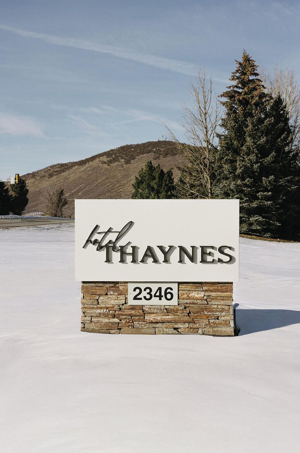 Um sinal para 'Haynes' com o número 2346, com paisagem nevada ao fundo, incluindo árvores e uma colina.
