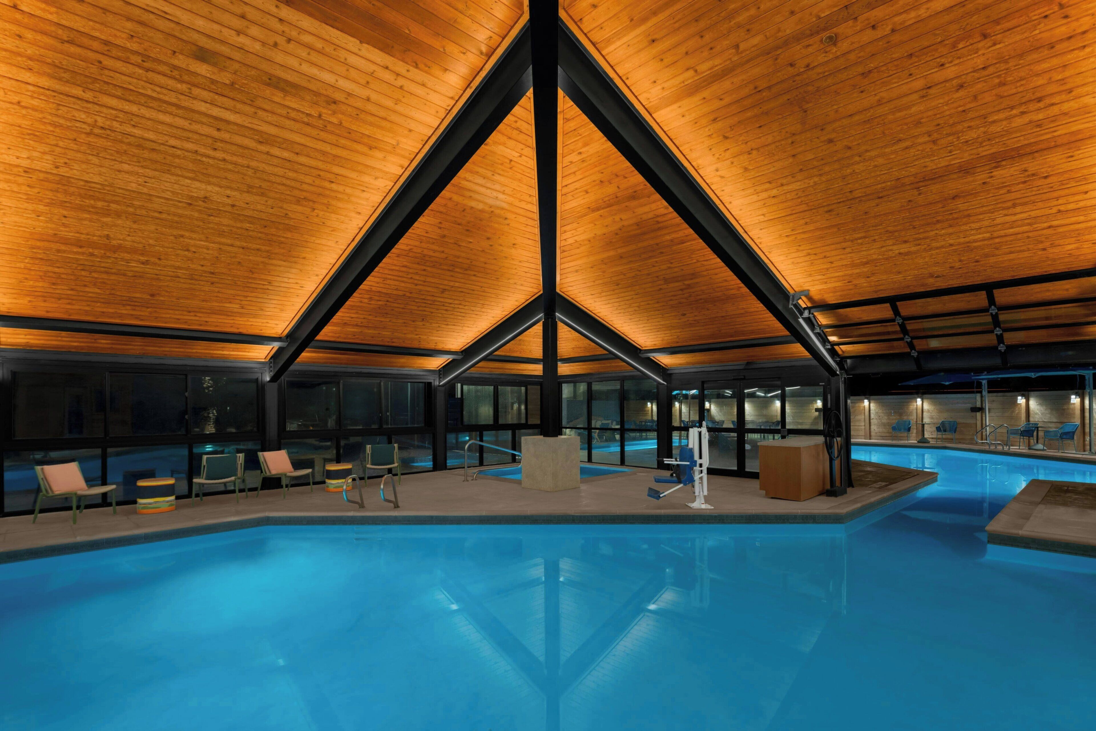 A modern indoor swimming pool with a wooden ceiling and glass walls.