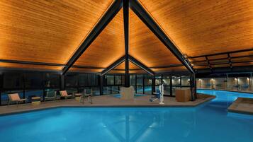A modern indoor swimming pool with a wooden ceiling and glass walls.