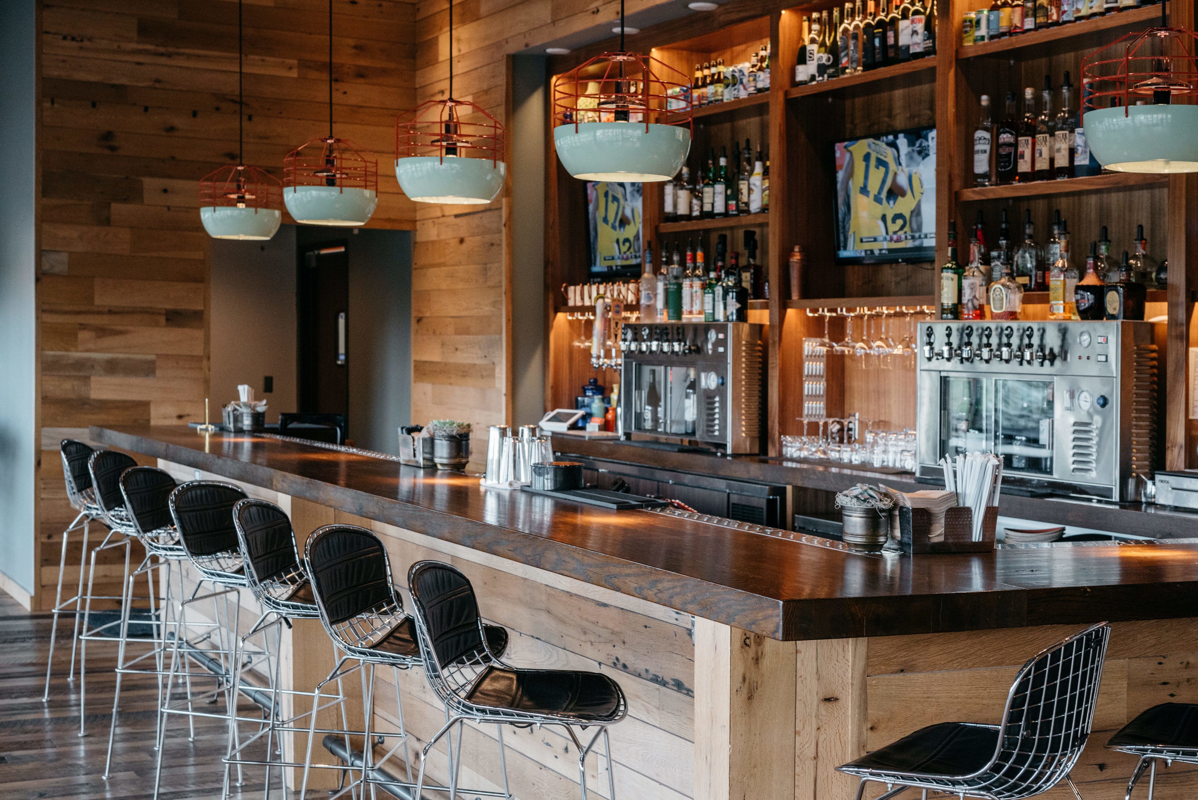 A bar area with a long counter, multiple stools, and a variety of bottles and glasses on shelves.
