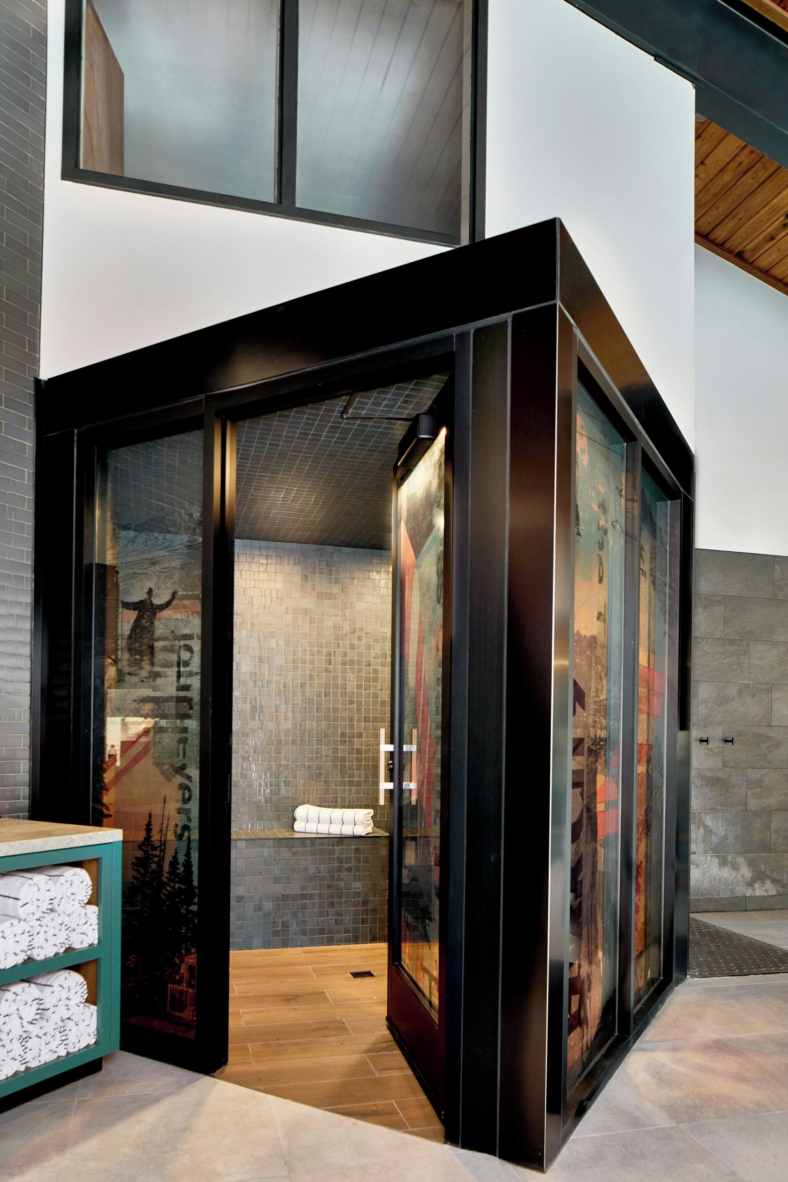 A modern bathroom with a glass enclosure, a wooden floor, and a tiled wall.