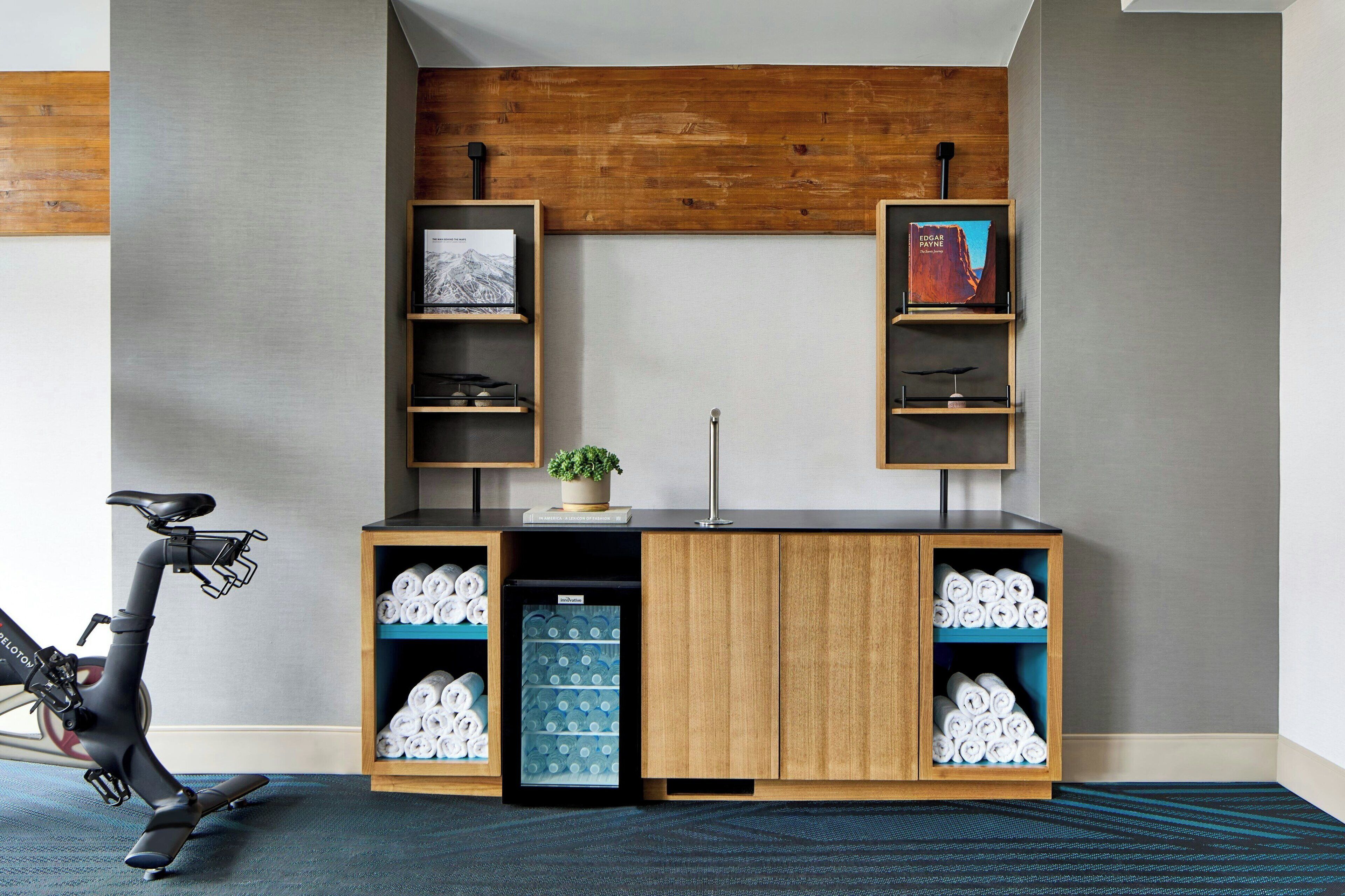 A modern room with a wooden cabinet, shelves with books, a small refrigerator, and a stationary bike.
