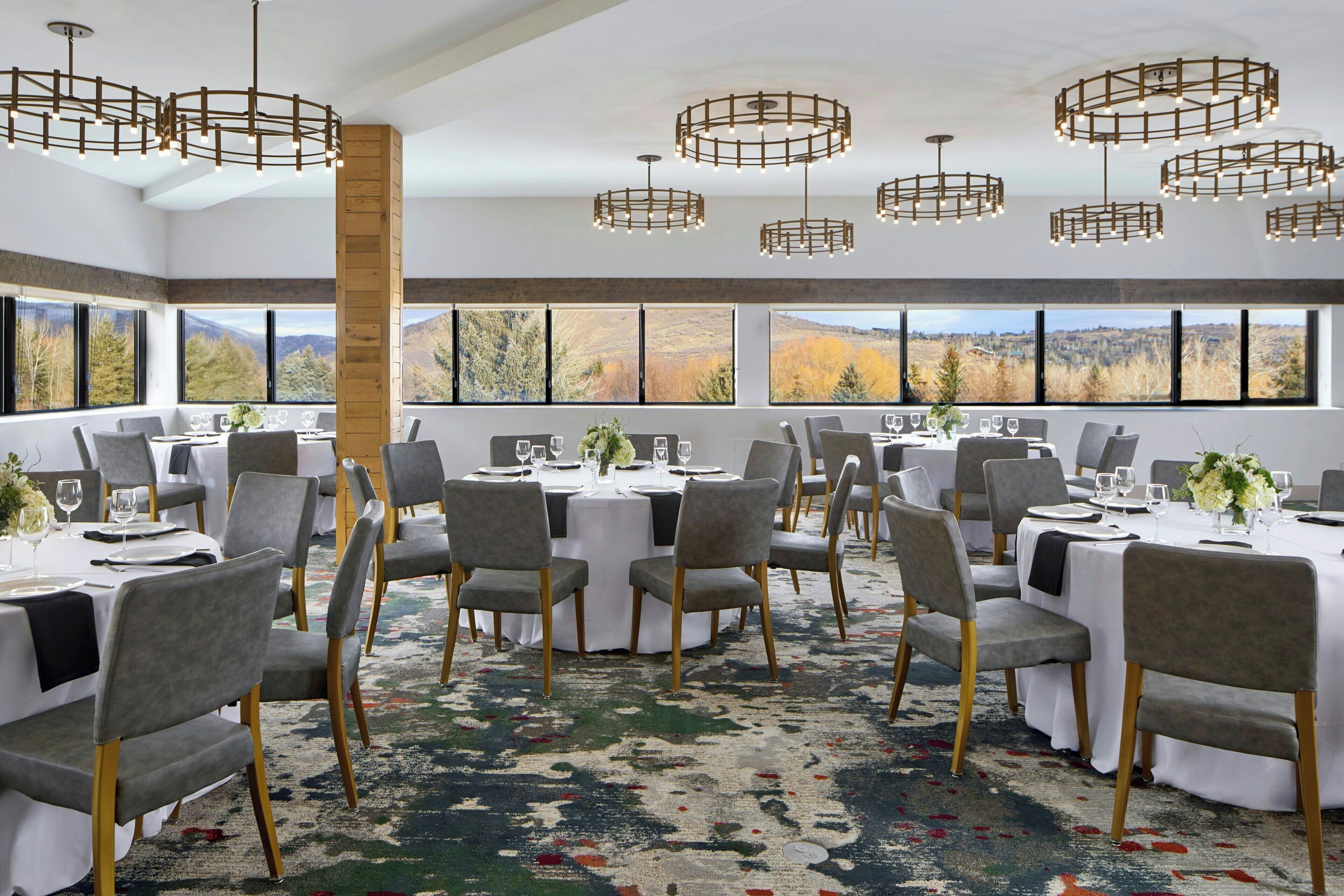 A dining area with round tables, grey chairs, and a large window with a mountain view.