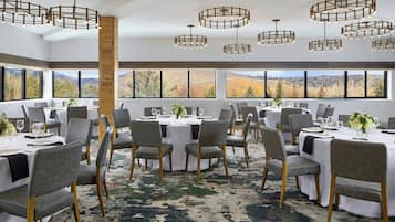 A dining area with round tables, grey chairs, and a large window with a mountain view.