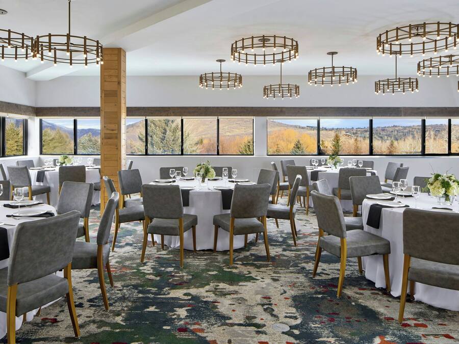 A dining area with round tables, grey chairs, and a large window with a mountain view.