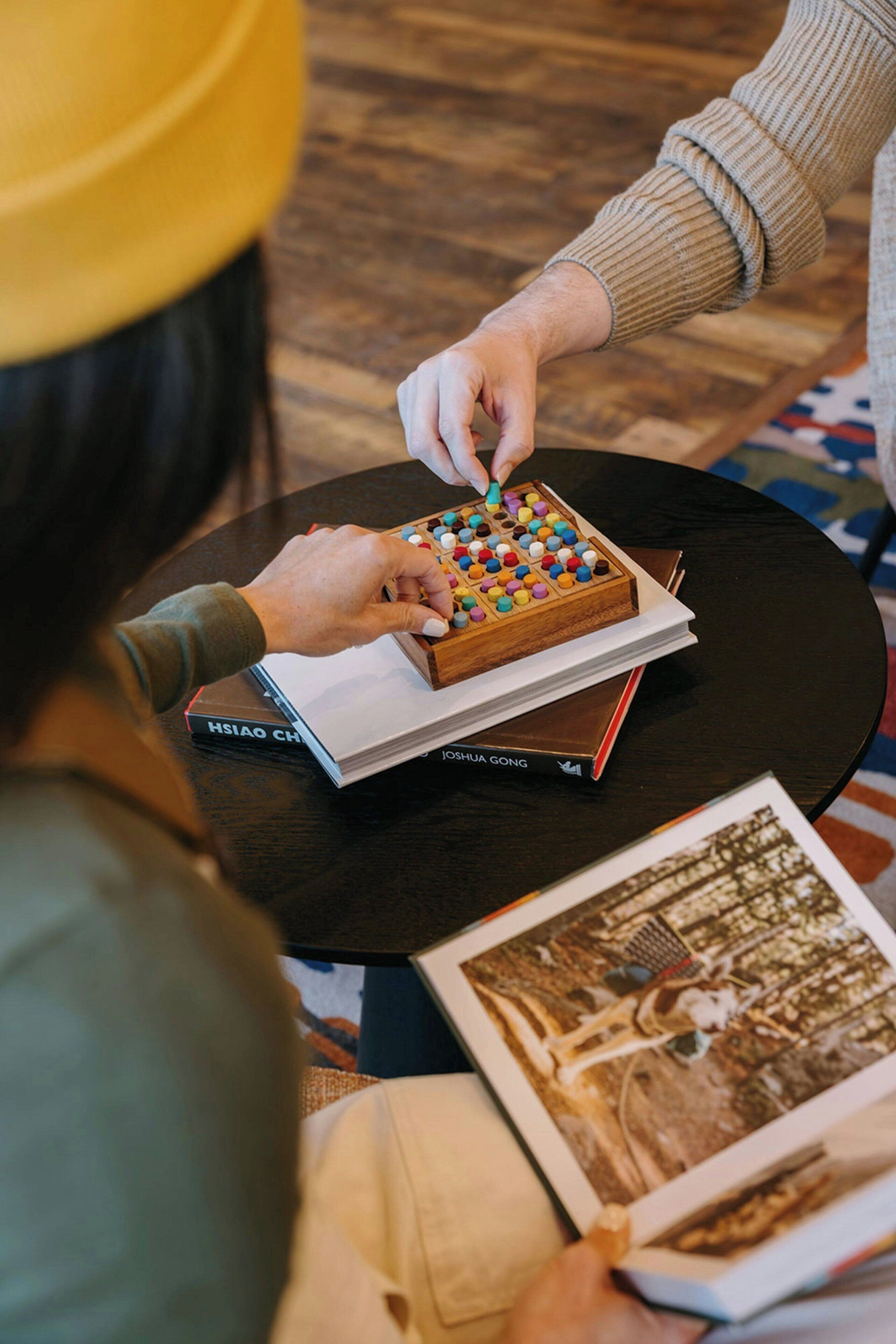 Una persona ordenando bloques de madera de colores sobre una mesa con libros y una fotografía.