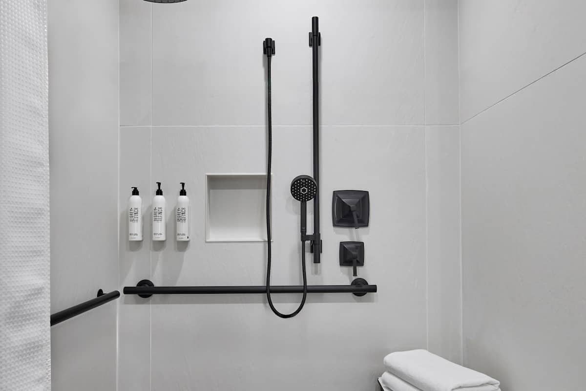 A modern shower area with a rain showerhead, handheld showerhead, and a handheld massage showerhead. There are three bottles of shampoo and conditioner on a shelf, and a towel rack with folded towels.