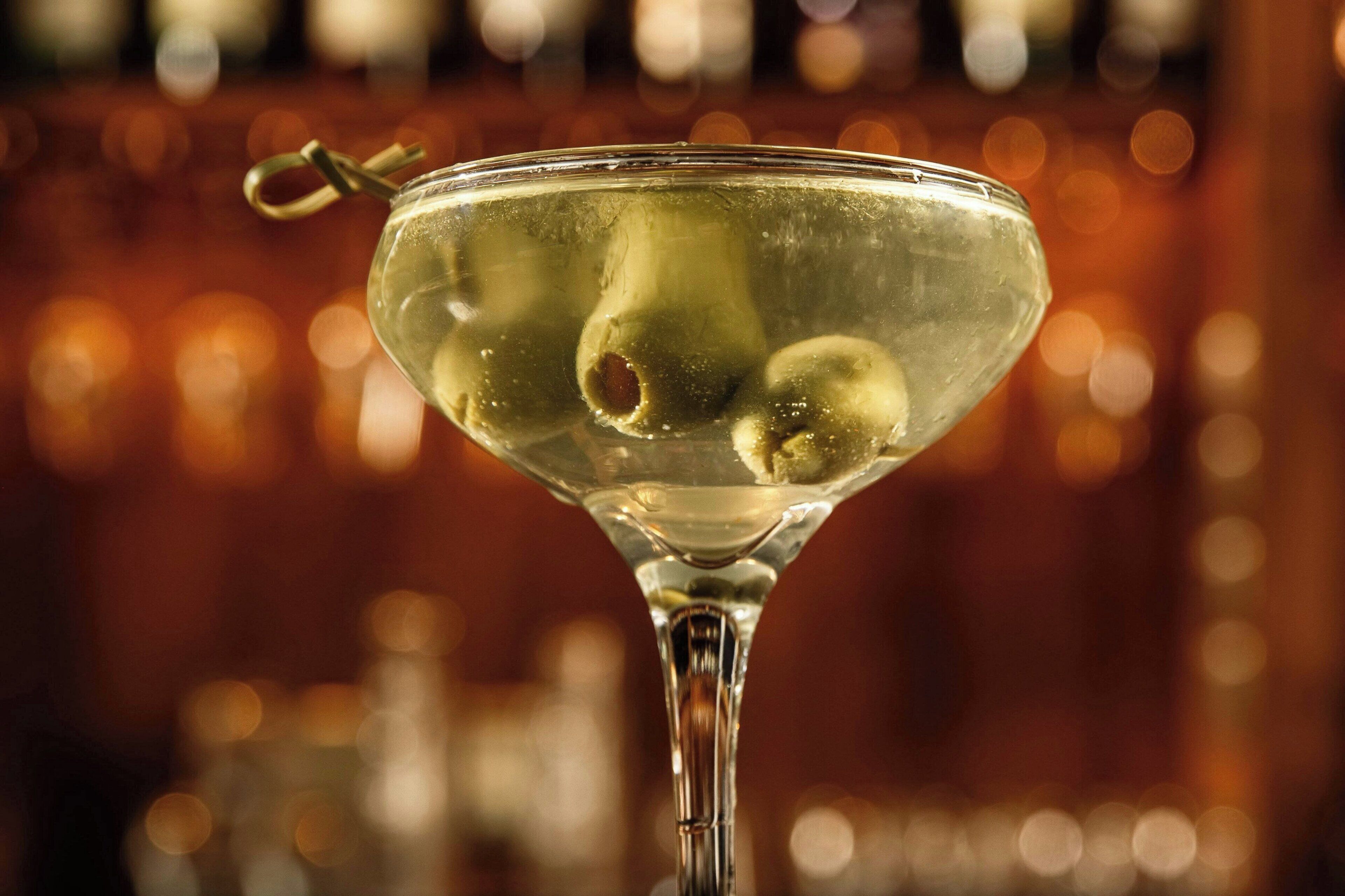 A martini glass with a lemon slice and olive on a bar counter.