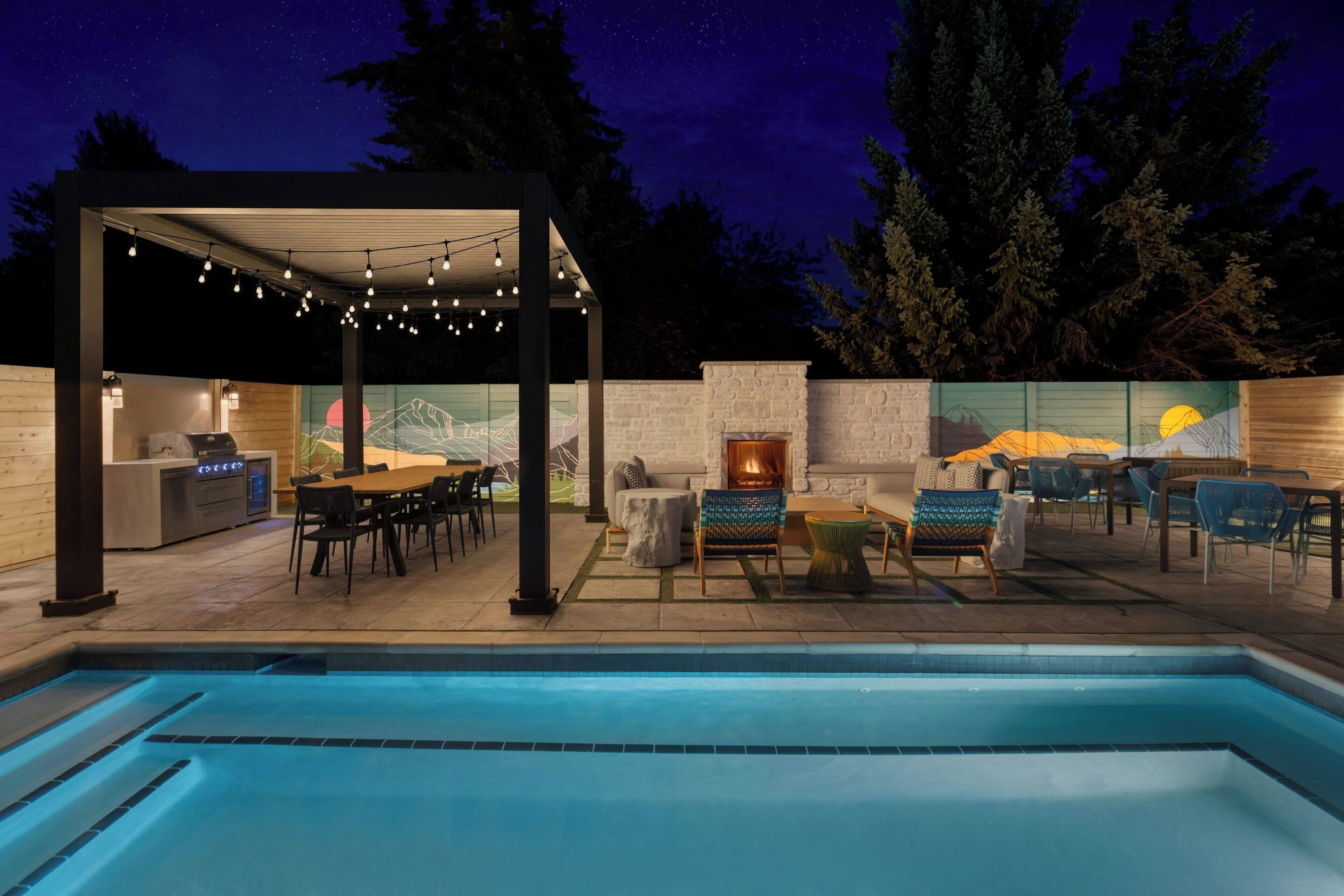 An outdoor pool area with a covered seating area, a barbecue grill, and a stone fireplace.