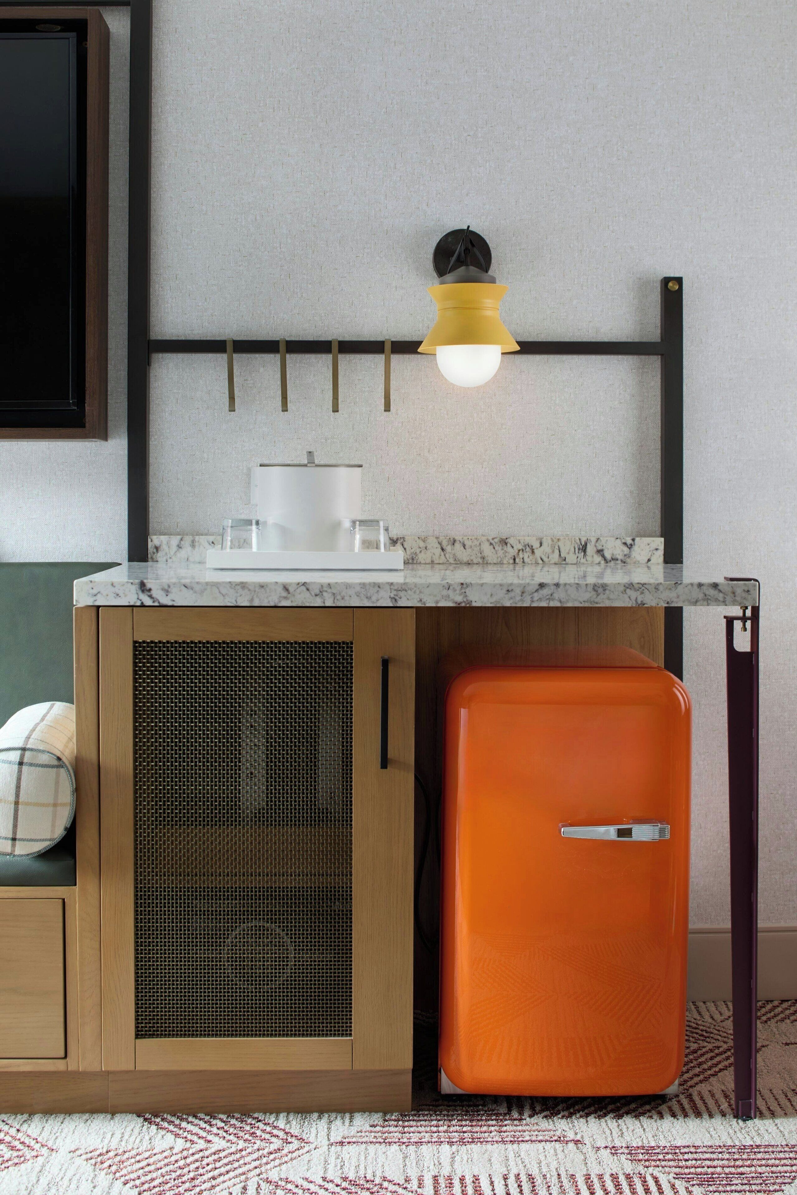 Une cuisine compacte dotée d’un plan de travail en marbre, d’un four encastré, d’un petit réfrigérateur orange et d’un luminaire fixé au mur.