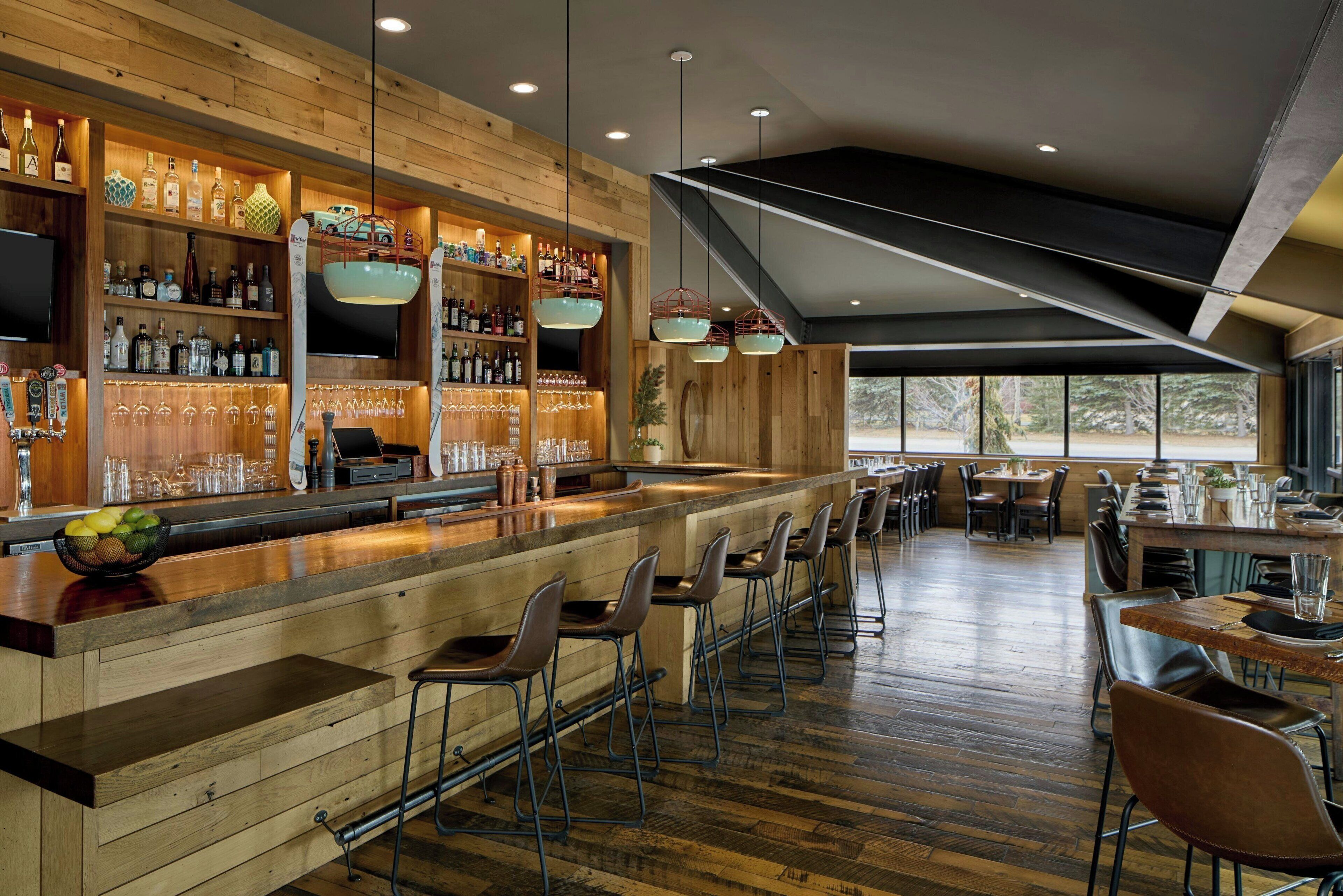 A bar area with wooden shelves, bar stools, and a variety of bottles and glasses.