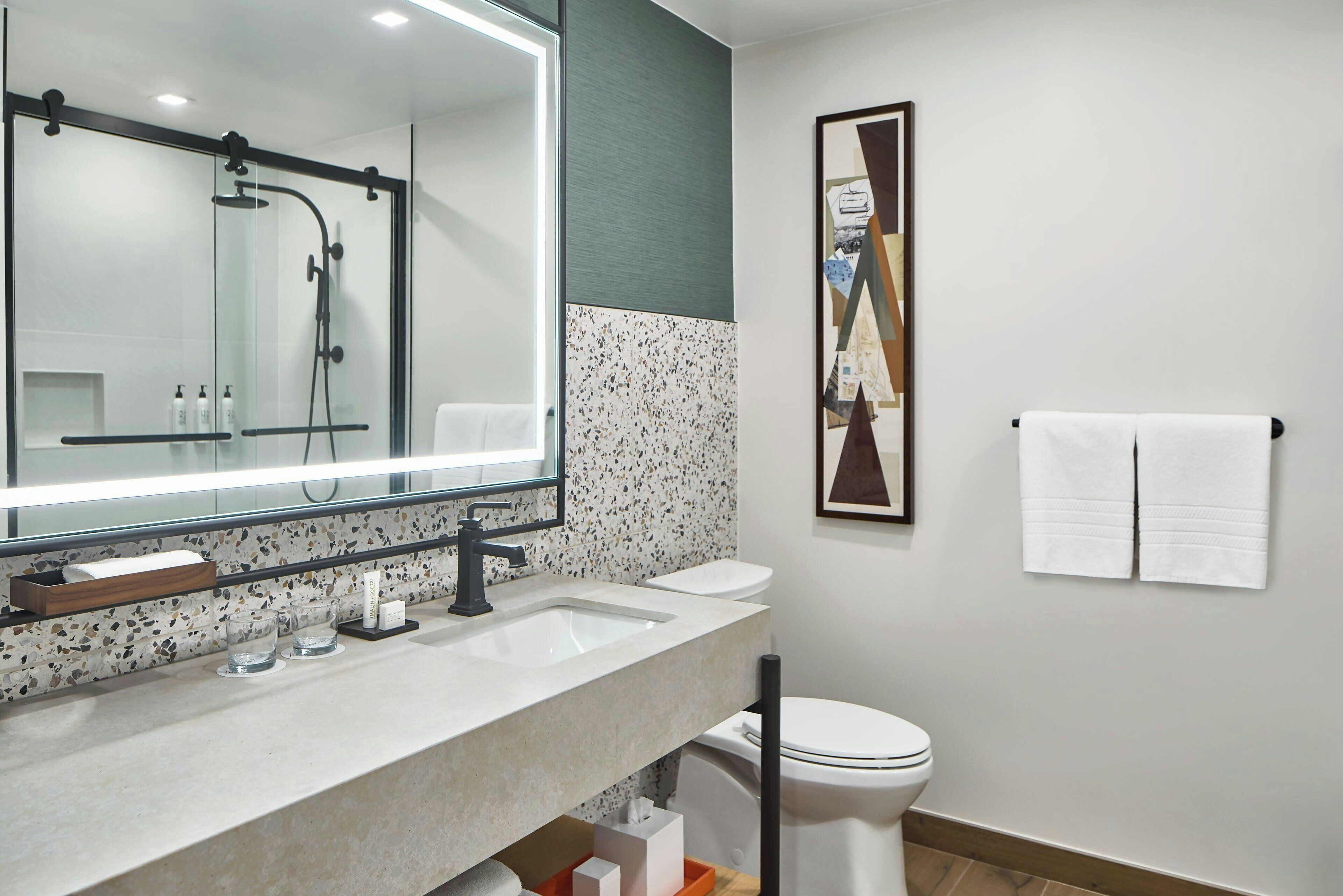 A modern bathroom with a glass-enclosed shower, a large mirror, a sink with a soap dispenser, and a toilet.