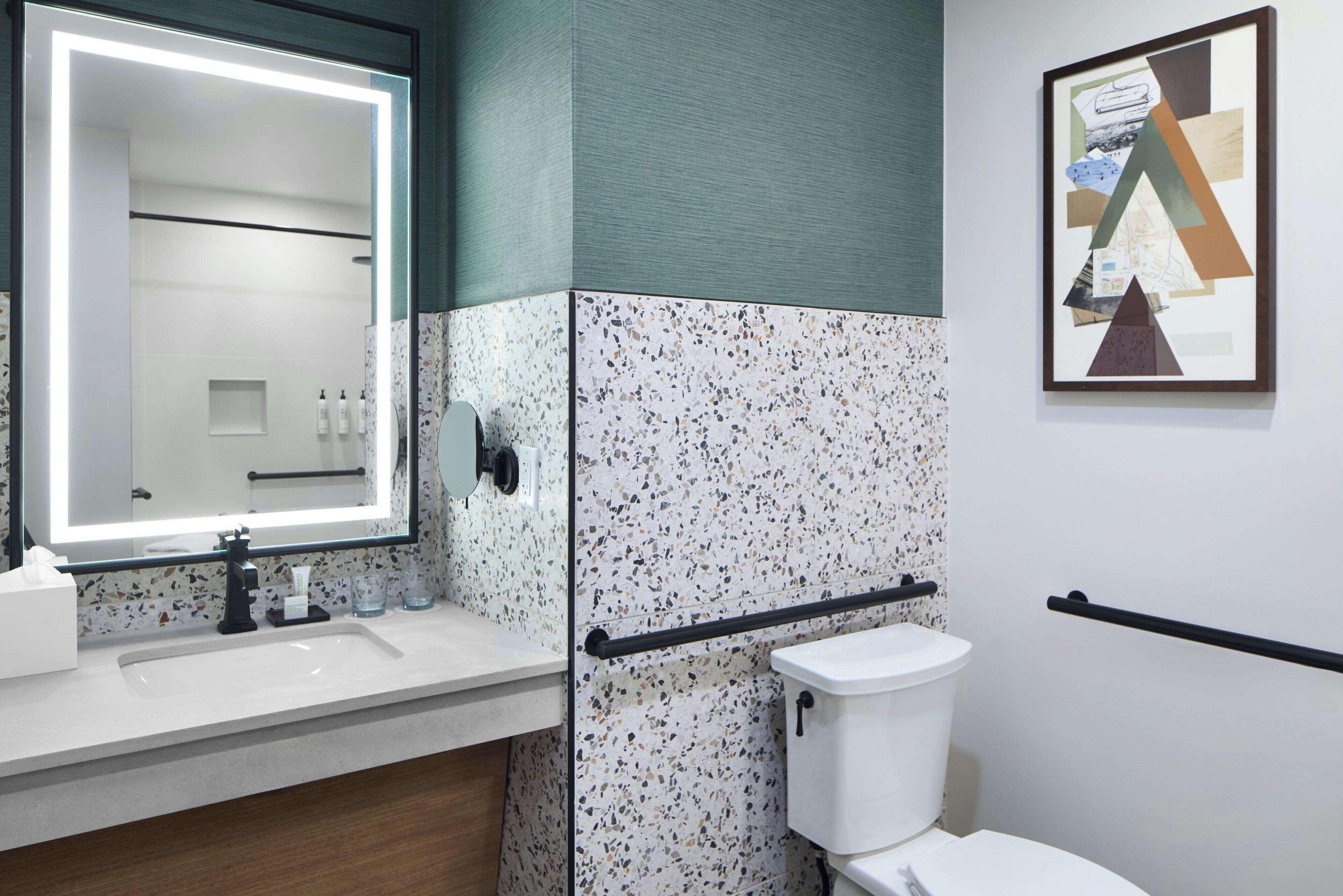 A modern bathroom with a white sink, a mirror with integrated lighting, a toilet, and a wall-mounted towel rack.
