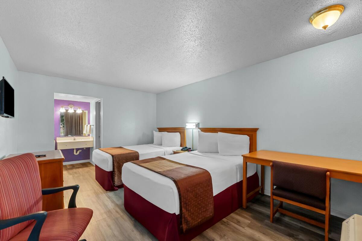 Een hotelkamer met twee bedden, een bureau, een stoel, een spiegel en een zichtbare badkamer door een open deur.