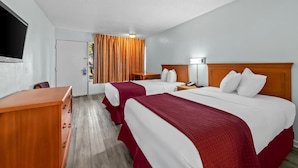 Ein Hotelzimmer mit zwei Betten, einem Holztisch, einem Fernseher und einem Fenster mit Vorhängen.