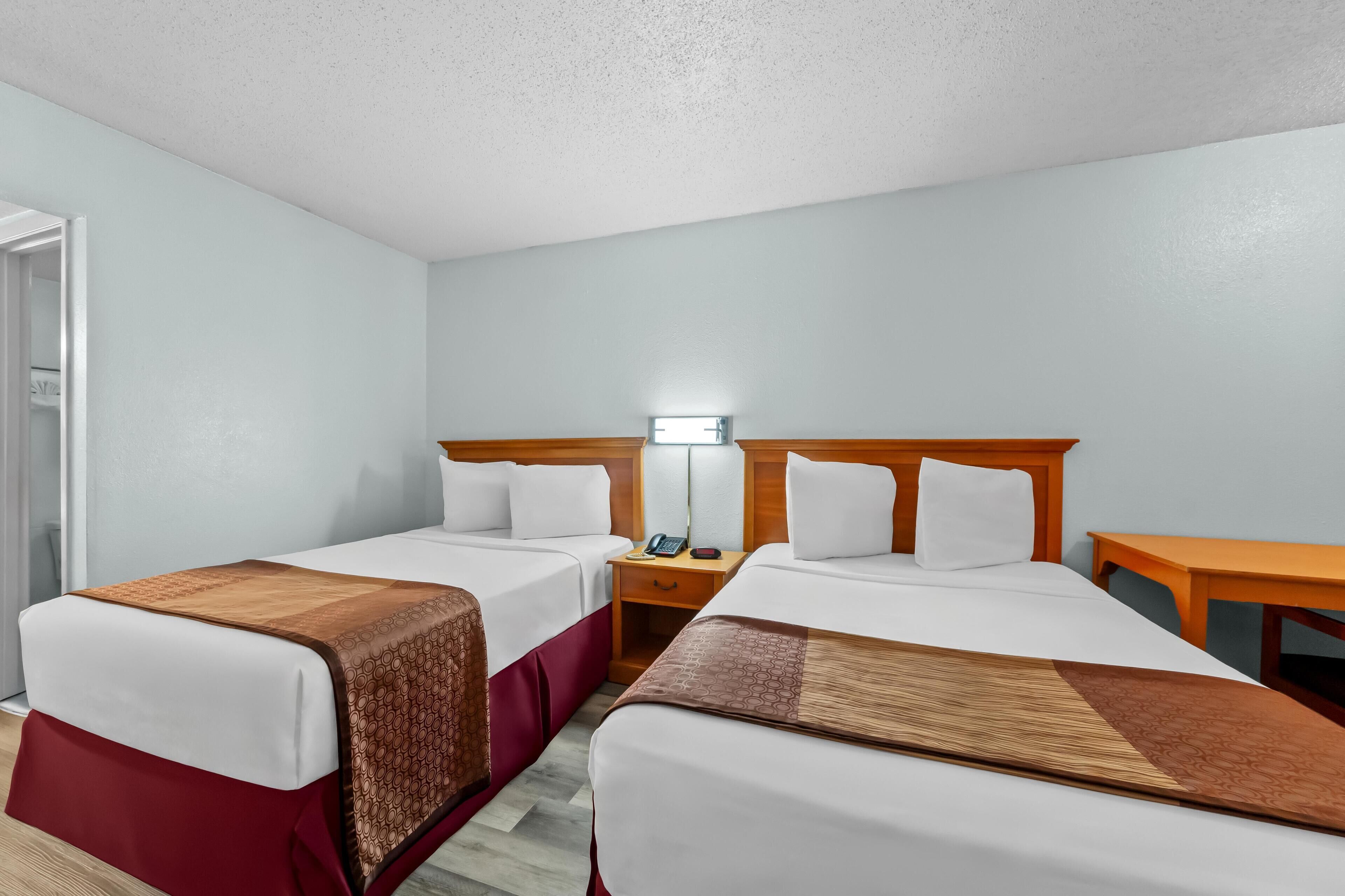 A hotel room with two beds, a nightstand with a lamp, and a wooden table.