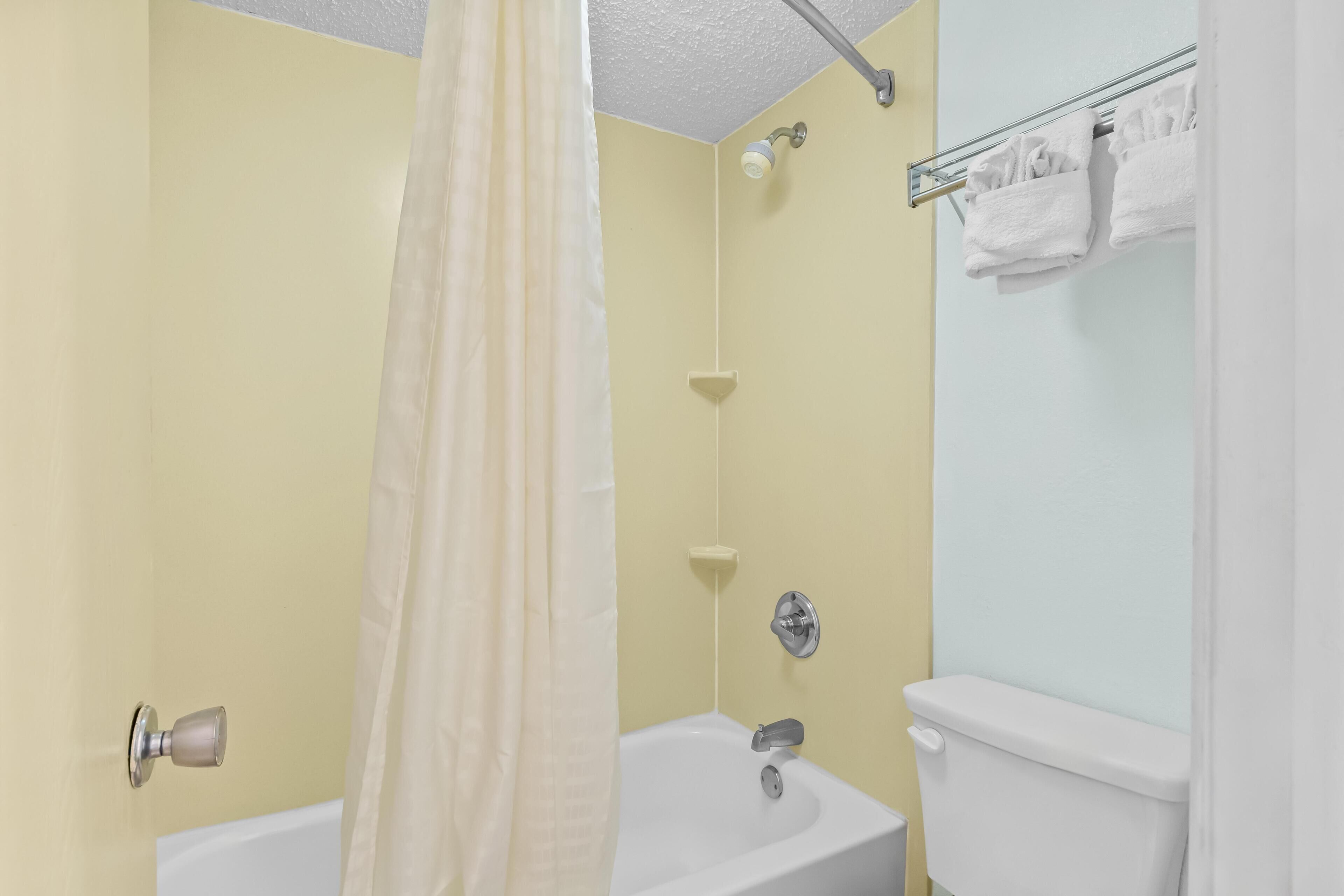 Un baño con bañera, cortina de ducha, toallero y retrete.