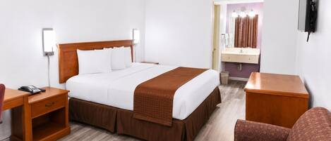 Habitación de hotel con cama, mesitas de noche, escritorio, silla, televisión y baño con espejo y cortinas.