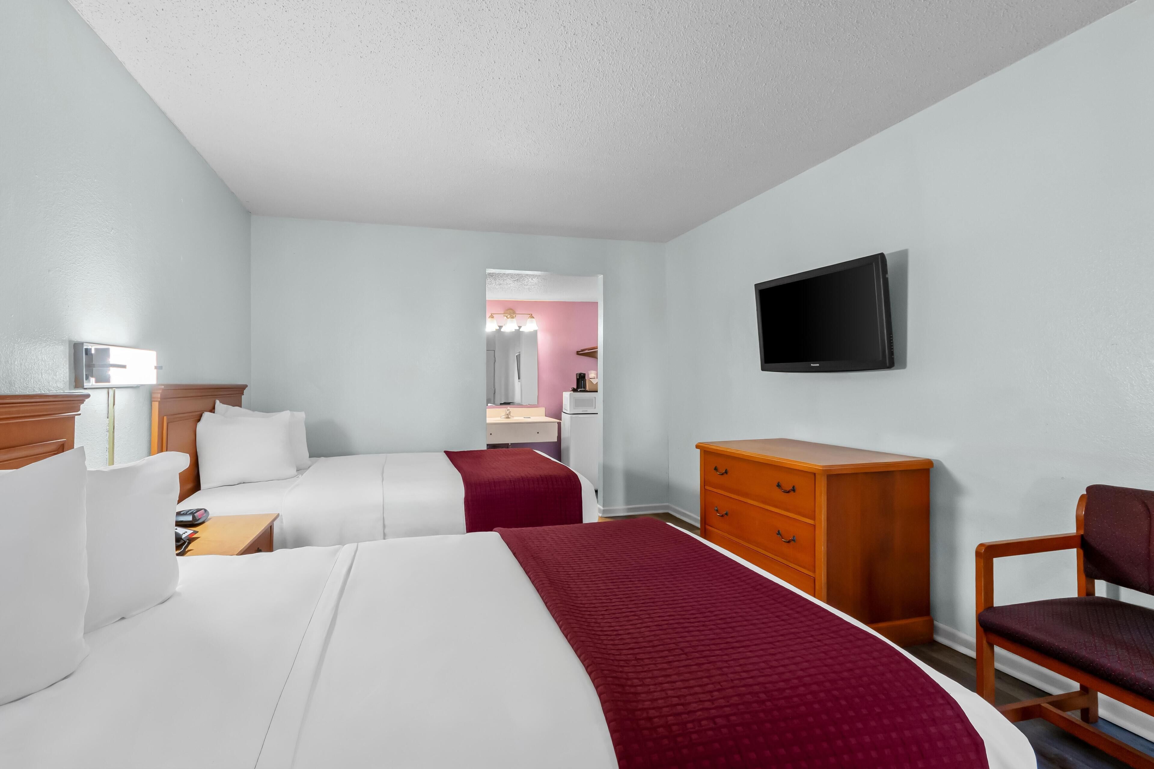 A hotel room with two beds, a wooden dresser, a television, and a chair.
