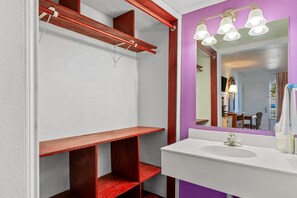 A bathroom with a white sink, a mirror with three lights, and wooden shelves.