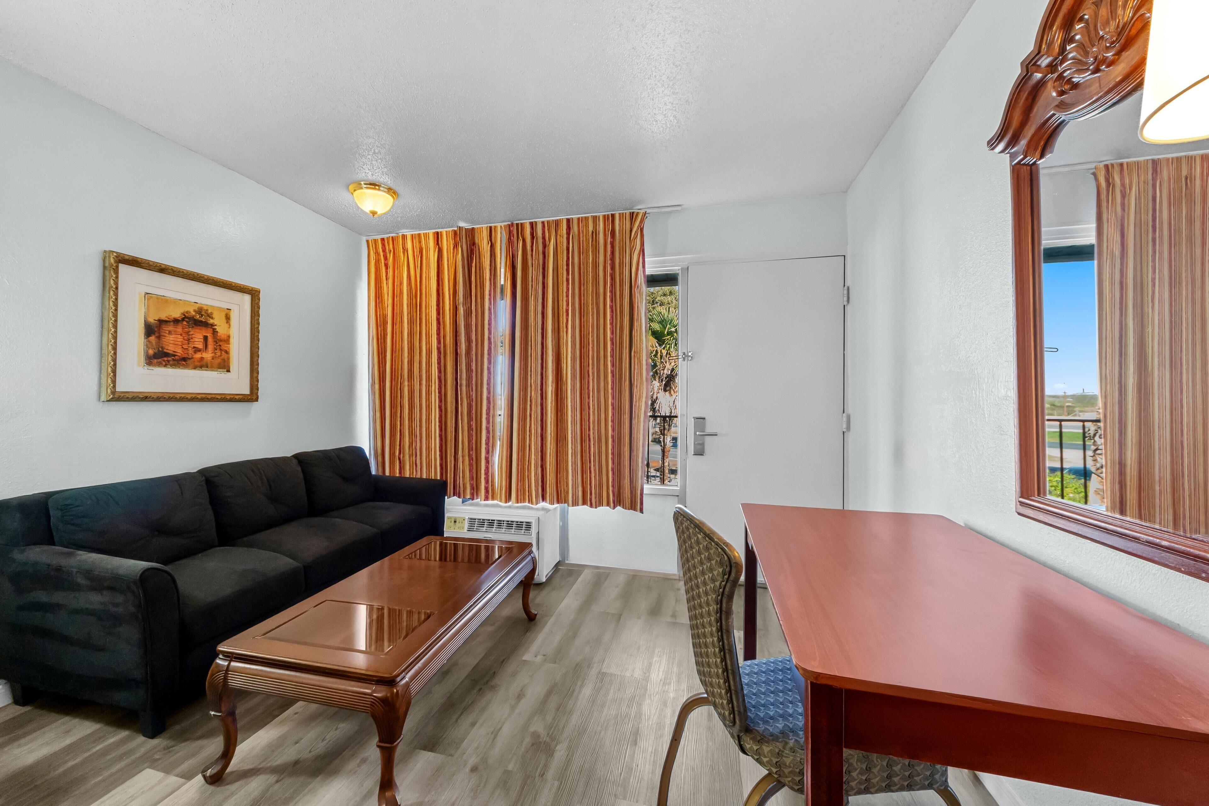 Une pièce avec un canapé de couleur sombre, une table basse en bois, une table à manger avec une chaise, et un grand miroir au mur.