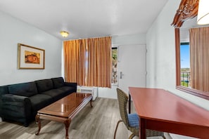 A room with a dark-colored sofa, a wooden coffee table, a dining table with a chair, and a large mirror on the wall. - Knights Inn San Antonio near Frost Bank Center (San Antonio)